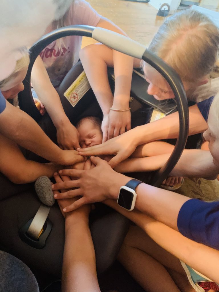 kids putting hands around baby in car seat